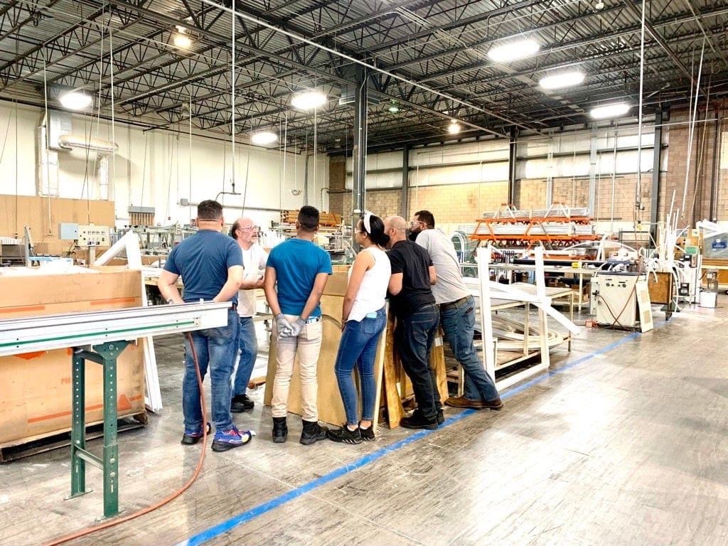 Workers receiving instruction around table in warehouse.