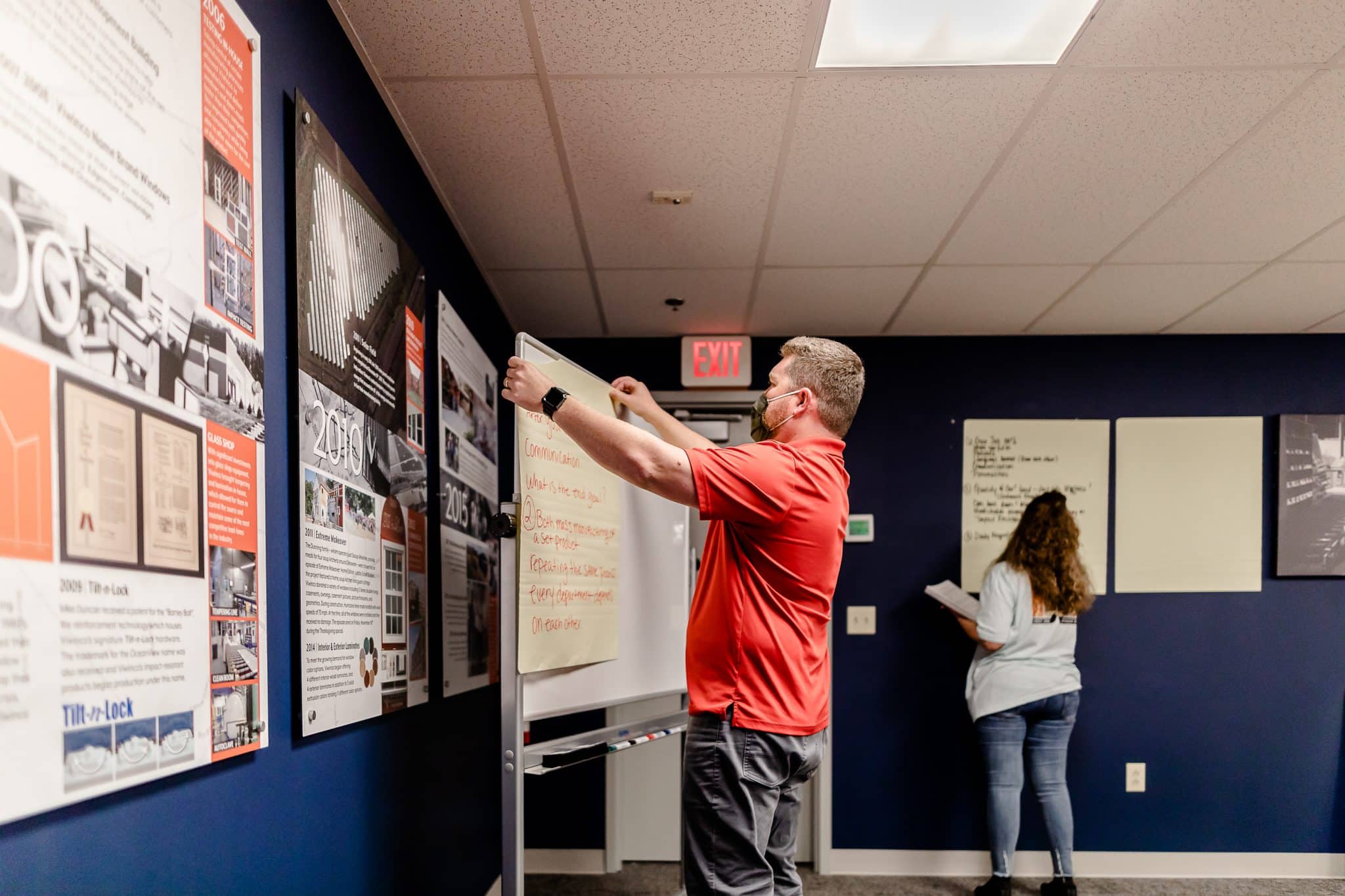 Man in red shirt posting paper onto whiteboard.