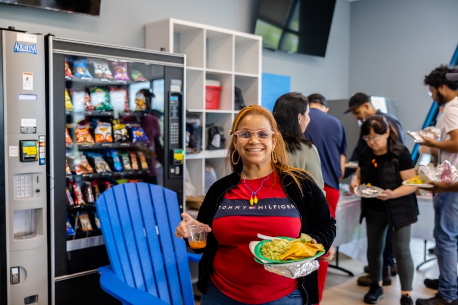 Portrait of woman holding a plate of food, wearing manufacturing PPE and smiling.