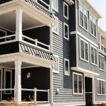 A modern multi-level building featuring dark blue siding and white trim. The structure has large windows and balconies, giving it a contemporary look.