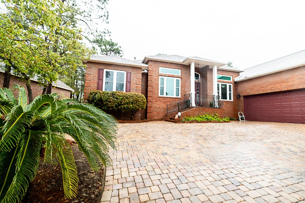 Hometown - Job 1 Web-47 A brick home with a large driveway made of stone pavers, featuring a front porch with columns and well-maintained greenery, including a large palm.